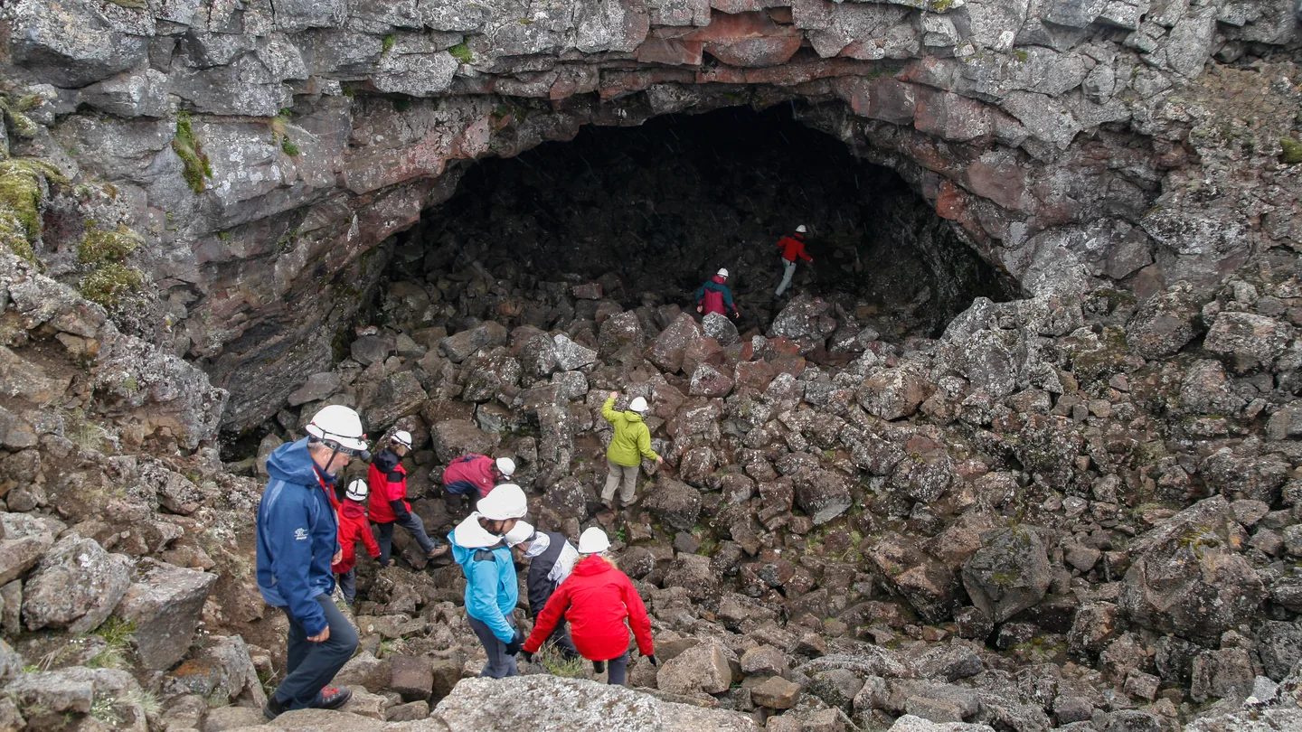 Visitors in helmets descending into the rocky entrance of Surtshellir lava cave in Iceland